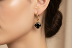 Gold earrings with black clover-shaped stones on a white background