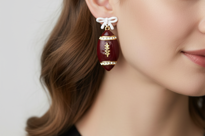 Football-shaped earrings with rhinestone details on a white background
