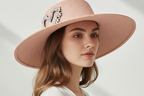 Pink straw hat with a decorative heart brooch on a white background