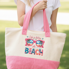 Person holding a tote bag with 'Life is better at the beach' text and sunglasses design.