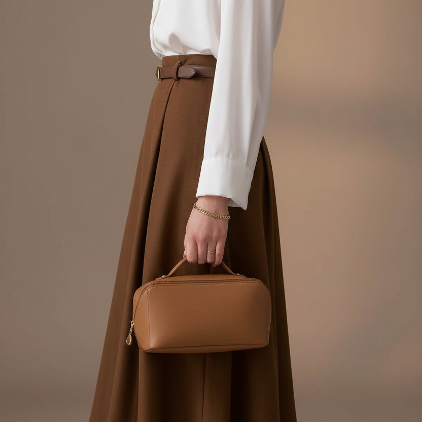 Person holding a brown leather handbag with a neutral background