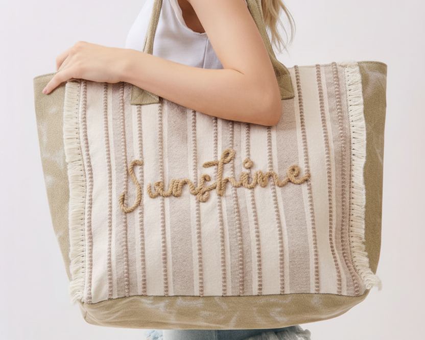 Person holding a striped tote bag with 'Sunshine' embroidery on a plain background