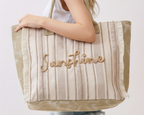 Person holding a striped tote bag with 'Sunshine' embroidery on a plain background