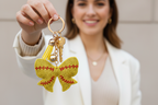 Yellow butterfly keychain with red details on a white background
