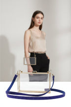 Clear handbag with gold frame and blue glittery strap on a white background